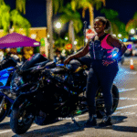 Shena Carty, motorcycle rider known as Showstopper, standing beside a black Suzuki Hayabusa at a bike night with other motorcycles in the background.